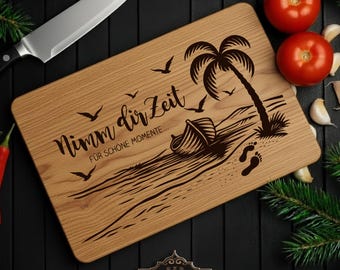 May include: Wooden cutting board with a beach scene engraved, including a palm tree, boat, footprints, and the text "Nimm dir Zeit". Includes a stainless steel knife, tomatoes, and garlic.