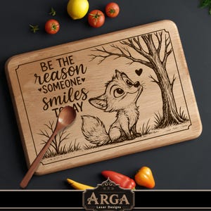 Puede incluir: Tabla de cortar de madera con un diseño grabado con láser que representa un zorro mirando hacia arriba a un árbol, con el texto "BE THE reason SOMEONE smiles TODAY". Incluye una cuchara de madera. Artículos de cocina decorativos.