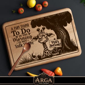 Puede incluir: Tabla de cortar de madera con una ilustración de jirafa y el texto "A FUN THING To Do IN THE Morning = IS NOT = Talk To Me". Una cuchara de madera y verduras rodean la tabla. La jirafa sostiene un letrero que dice "YUR'S AWESOME!"