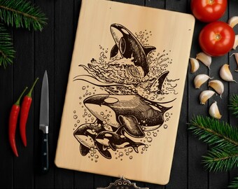 May include: A rectangular wooden cutting board with a laser-etched design of orcas swimming in the ocean. The design includes three orcas, water, and bubbles. The board is surrounded by tomatoes, garlic, and chili peppers. The text "ARGA Laser Designs" is at the bottom.