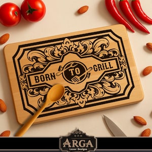 Könnte beinhalten: Rechteckiges Holzschneidebrett mit dem Schriftzug "BORN TO GRILL" in Schwarz. Das Brett hat einen schwarzen Rand und ein zentrales kreisförmiges Design mit Gabel und Hammer. Rote Tomaten, Chilischoten, Mandeln und ein Holzlöffel sind um das Brett angeordnet.