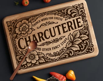 May include: Wooden charcuterie board with engraved floral design and the word "CHARCUTERIE". The board includes the text "French word for cheese" and "and other fancy stuff". A wooden spoon rests on the board, with tomatoes, peppers, and a lemon nearby.