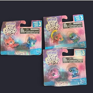 Puede incluir: Tres paquetes de juguetes Littlest Pet Shop. Cada paquete contiene dos pequeñas figuras de animales coloridas. El embalaje es una mezcla de morado, azul y rosa con las palabras "Littlest Pet Shop" y "Serie 3" impresas. La etiqueta de advertencia dice "Peligro de asfixia - Piezas pequeñas."