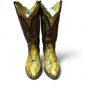 May include: A pair of cowboy boots featuring a yellow snakeskin pattern on the foot and a brown leather shaft. The boots have a pointed toe and a tall, angled shaft with decorative stitching. The top of the shaft is trimmed with yellow leather.