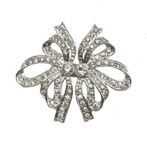 May include: A silver bow brooch with clear rhinestones. The bow is made of metal and has a delicate design.