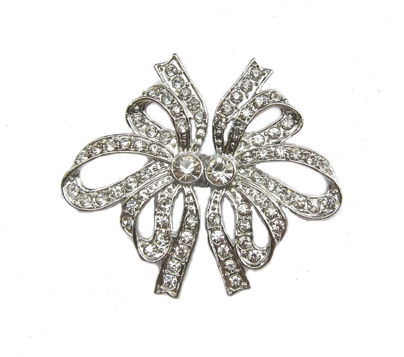 May include: A silver bow brooch with clear rhinestones. The bow is made of metal and has a delicate design.