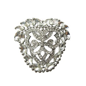 Op de afbeelding: Een zilveren broche met een hartvormig ontwerp, met een delicaat filigraanpatroon en heldere strasssteentjes.