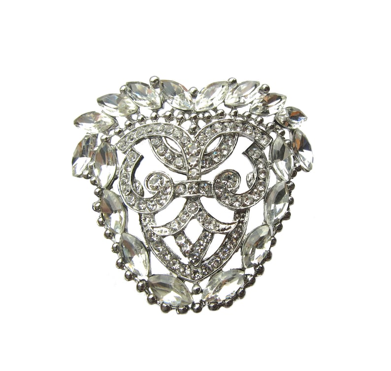 Op de afbeelding: Een zilveren broche met een hartvormig ontwerp, met een delicaat filigraanpatroon en heldere strasssteentjes.