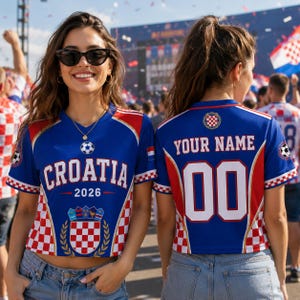 Two women wearing blue and red Croatia soccer jerseys with the text "CROATIA 2026" and "YOUR NAME 00" printed on them, standing in front of a crowd.