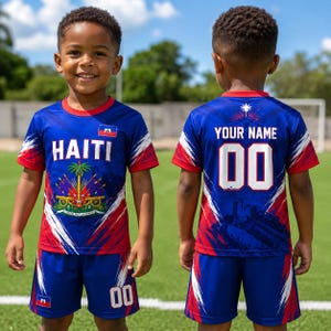 A young boy wearing a blue and red sports jersey with the word "HAITI" printed on it, standing on a soccer field.