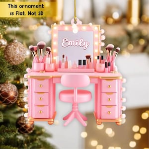 May include: A pink vanity ornament with a lighted mirror, makeup brushes, and cosmetics. The vanity has drawers and a matching stool. The name "Emily" is written on the mirror. The ornament is flat, not 3D.