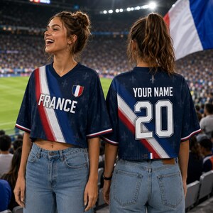 Two women wearing blue and red France-themed soccer jerseys with the number 20, smiling and standing in a stadium.