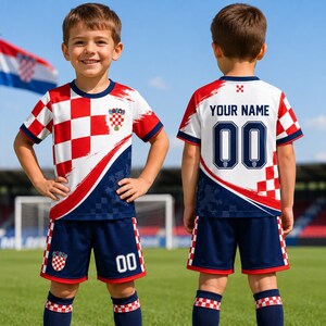 A young boy wearing a red and white soccer uniform with the number 00 and the name "YOUR NAME" printed on the back, standing on a soccer field.