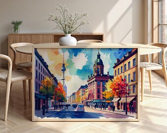 May include: A framed watercolor print of a city street scene. The artwork depicts buildings, trees with autumn foliage, and a distant tower. The color palette includes blues, yellows, and reds, creating a vibrant and artistic representation of urban life.