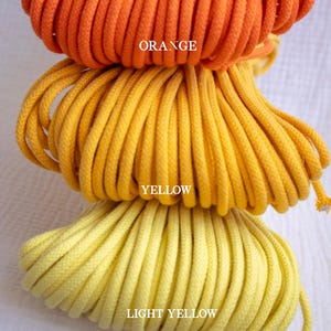 May include: Three spools of rope in shades of orange, yellow, and light yellow are stacked. The word "ORANGE" is printed on the top spool. The word "YELLOW" is printed on the middle spool. The word "LIGHT YELLOW" is printed on the bottom spool.