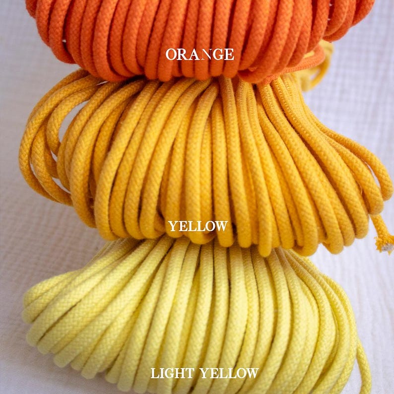 May include: Three spools of rope in shades of orange, yellow, and light yellow are stacked. The word "ORANGE" is printed on the top spool. The word "YELLOW" is printed on the middle spool. The word "LIGHT YELLOW" is printed on the bottom spool.