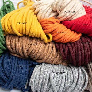 May include: A selection of macrame cords in a variety of colours, such as green, yellow, natural, red, orange, caramel, maroon, blue, stone grey, and latte. The cords are tightly wound and labelled with their respective colours.
