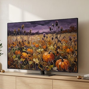 Op de afbeelding: Een flatscreen-televisie met een olieverfschilderij van een veld vol oranje pompoenen en hoge distels met paarse toppen onder een donkere, sfeervolle lucht, geplaatst op een mediameubel van licht hout.