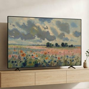 May include: A flat-screen television displaying an impressionist landscape painting of a field with orange and blue wildflowers under a cloudy sky, mounted above a light-toned wooden floating media console with three drawers and a small vase.