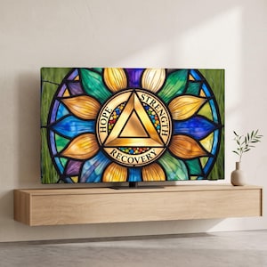 May include: A flat-screen television displaying a stained-glass style graphic with a central gold triangle. The text HOPE, STRENGTH, and RECOVERY is printed around the triangle, surrounded by a colorful floral pattern in blue, green, and yellow.