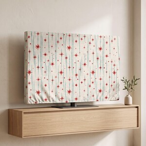 May include: A rectangular television cover featuring an off-white background with a repeating pattern of vertical teal lines and small red starburst shapes. The fabric cover is fitted over the screen of a flat-panel television.