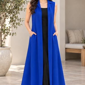 Puede incluir: Un chaleco largo sin mangas de color azul real con cuello de solapa y dos bolsillos laterales, usado sobre un vestido negro sencillo hasta el suelo. El chaleco largo abierto por delante crea una silueta superpuesta de diseño liso.