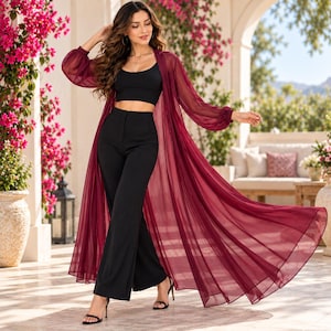 Peut inclure: Un ensemble trois pièces composé d'un haut court noir à encolure dégagée, d'un pantalon noir taille haute à jambes larges et d'un long gilet transparent bordeaux avec de longues manches bouffantes, ouvert sur le devant sur l'ensemble noir.