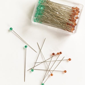 long and sharp sewing pins with green and amber colored heads