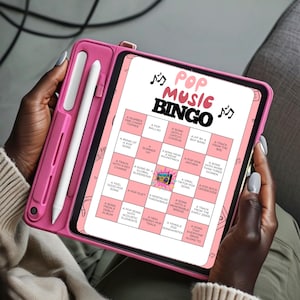 May include: A pink tablet with a Pop Music Bingo game displayed on the screen. The game board features various music-related prompts. A pink stylus is attached to the tablet case. The tablet is held by a person.