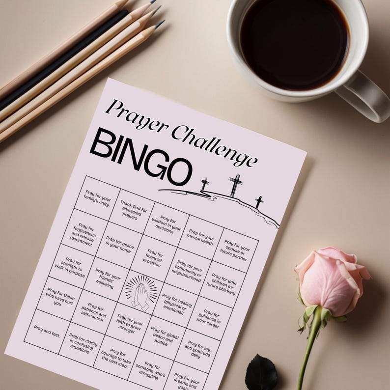 May include: A light pink "Prayer Challenge BINGO" game card with a black title and grid. The card includes various prayer prompts. A cup of coffee, pencils, and a pink rose are also in the image.