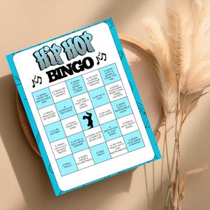 Op de afbeelding: Een Hip Hop Bingo-spelkaart met een lichtblauwe rand en een wit raster. De kaart bevat verschillende hiphop-thema's, waaronder songtitels en artiestenreferenties. De titel "Hip Hop Bingo" staat bovenaan, met muzieknoten.
