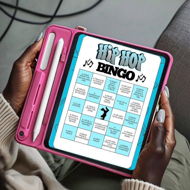Op de afbeelding: Een roze tablethoes bevat een tablet met een "Hip Hop Bingo"-spel. Het spelbord bevat verschillende muziekgerelateerde prompts. Een witte stylus is in de hoes geplaatst. De tablet wordt vastgehouden door een persoon met een donkere huid.