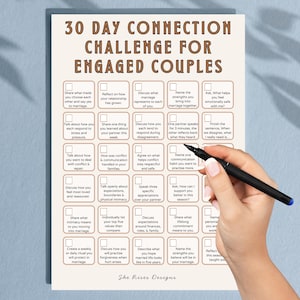 Puede incluir: Un desafío de conexión de 30 días para parejas comprometidas, con preguntas para fomentar la comunicación y la intimidad. El papel beige tiene una cuadrícula de casillas con preguntas como "Comparte lo que significa la intimidad para ti". Una mano sostiene un bolígrafo negro.
