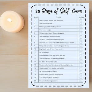 May include: A white candle with a lit wick sits next to a light blue self-care checklist. The checklist is titled "20 Days of Self-Care" and includes tasks like "Start a vision board" and "Go to bed early."