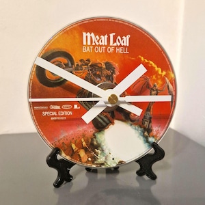 May include: A clock made from a CD, displaying the album art for Meat Loaf's "Bat Out of Hell." The clock has white hands and a gold centre, presented on a black stand. The CD art is mainly red and orange.