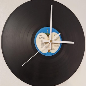 May include: A wall clock crafted from a black vinyl record featuring a central blue label with an apple graphic and the text The Beatles 1967-1970 Side Four. The clock has three thin white hands positioned at the centre of the record.