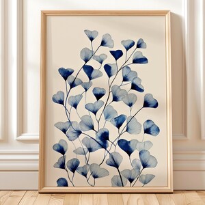 Può includere: Una stampa artistica incorniciata con un'illustrazione botanica di foglie di ginkgo blu su sfondo crema. Le foglie hanno un design lineare dettagliato e sono disposte in una composizione naturale e fluida. La cornice è di colore legno chiaro.