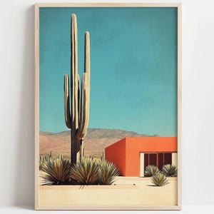 Può includere: Stampa artistica incorniciata raffigurante un paesaggio desertico con un grande cactus saguaro, un edificio arancione e un cielo blu. L'opera d'arte ha uno stile minimalista con un'estetica moderna della metà del secolo. La stampa è in una cornice di legno.
