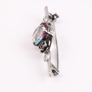 May include: Silver brooch with a large iridescent gemstone surrounded by a floral design.