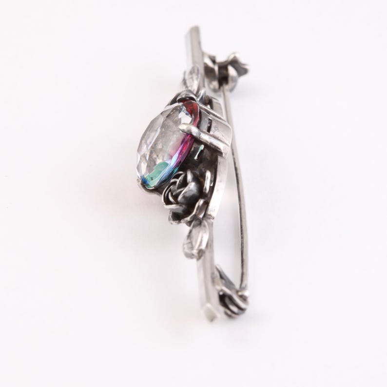 May include: Silver brooch with a large iridescent gemstone surrounded by a floral design.