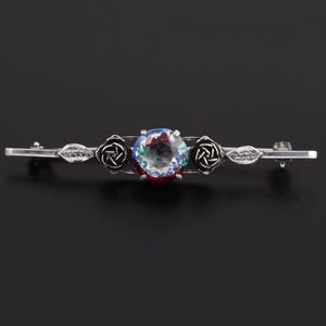 May include: A silver brooch with a large, faceted, clear gemstone surrounded by two silver rose motifs. The brooch has a delicate, vintage style.