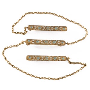 May include: Three gold-tone bar brooches with a delicate floral design in blue enamel. The brooches are connected by a gold-tone chain.