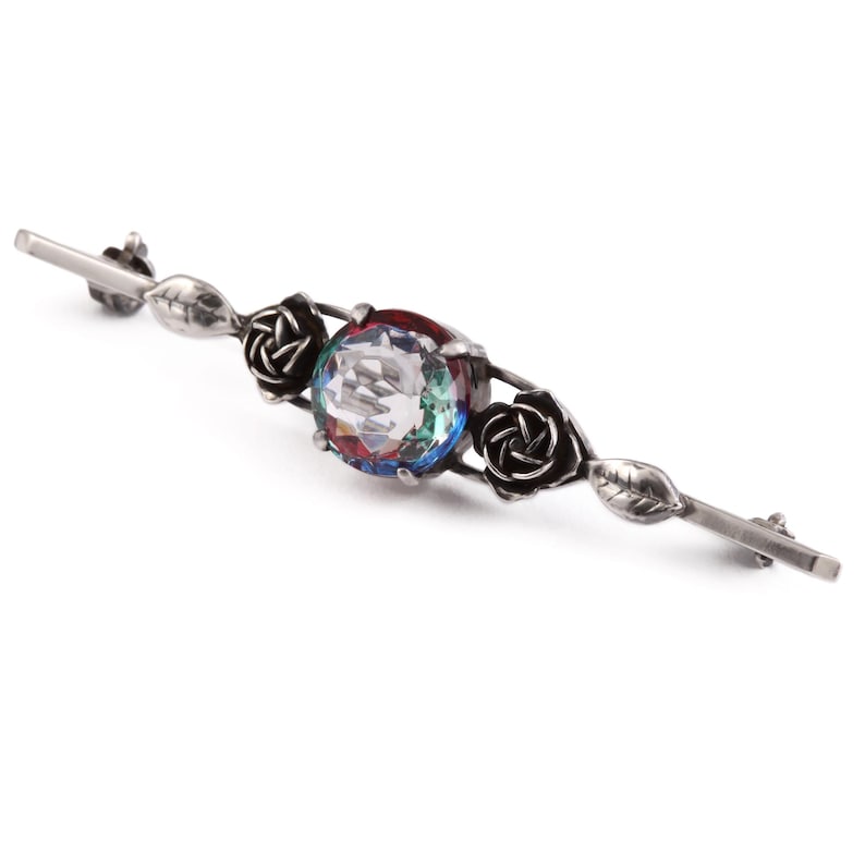 May include: Silver brooch with a large iridescent gemstone surrounded by three black rose accents.