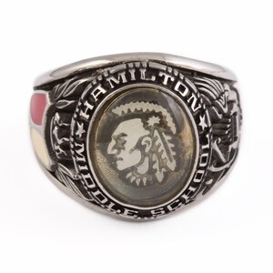 May include: A silver class ring with a red, white, and yellow enamel design. The ring features the words "Hamilton Middle School" and a Native American head in profile.