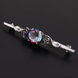 May include: A silver brooch with a large, round, iridescent gemstone surrounded by three silver rose motifs.