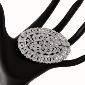 K&ouml;nnte beinhalten: Eine ovale Brosche aus Silber mit einem floralen Design, besetzt mit klaren Strasssteinen.