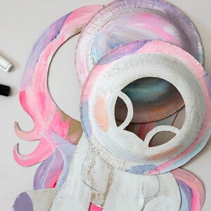 May include: A whimsical unicorn mask crafted from paper plates, painted with pastel pink, purple, and blue hues. The mask features cut-out eye holes and a white base, with a flowing mane and horn details. A creative craft project.