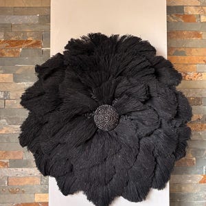 May include: A large, round, black wall hanging with a textured, layered design. The center features a circular, beaded embellishment. This decorative piece adds a touch of modern elegance to any interior space.