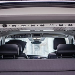 Könnte beinhalten: Innenansicht eines Fahrzeugs mit einem silbernen Gepäckträger über dem Kopf. Der Träger ist an der Decke befestigt und hat ein gitterartiges Design. Schwarze Kopfstützen und eine Rücksitzbank sind sichtbar.