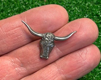 May include: A silver-toned metal bull head charm with detailed horns and a textured face.